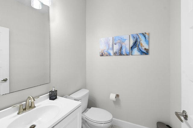 half bath featuring baseboards, vanity, and toilet