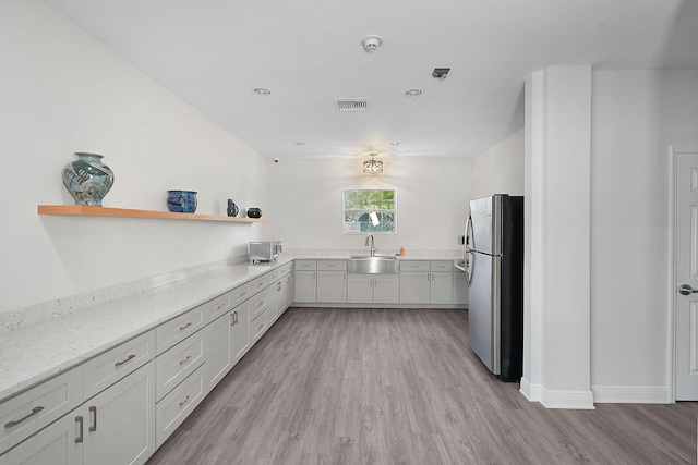 kitchen featuring visible vents, freestanding refrigerator, light wood-type flooring, open shelves, and a sink