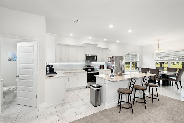 kitchen featuring a center island with sink, stainless steel appliances, visible vents, a sink, and a kitchen breakfast bar