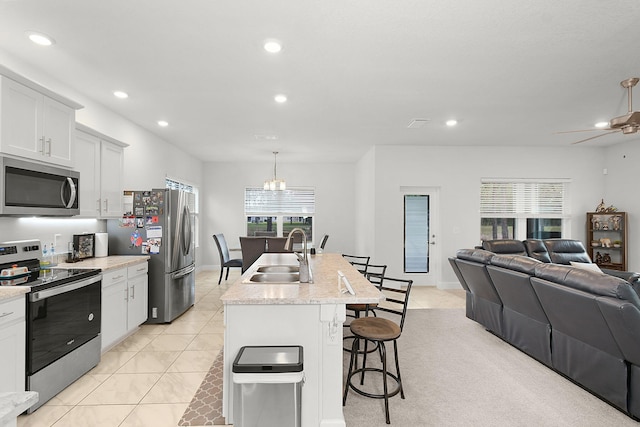 kitchen with light tile patterned floors, stainless steel appliances, open floor plan, a sink, and a kitchen breakfast bar