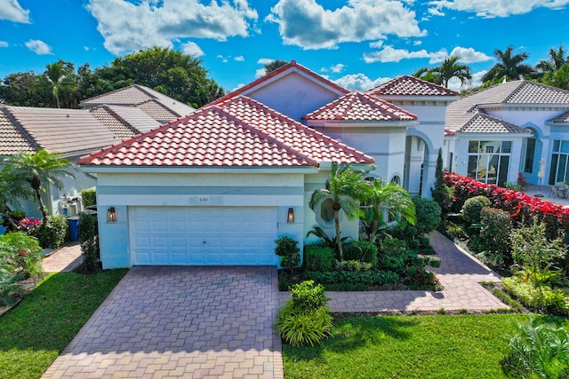 mediterranean / spanish house featuring an attached garage, a tile roof, decorative driveway, and stucco siding