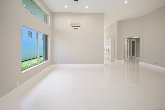 empty room with light tile patterned floors, a high ceiling, baseboards, and recessed lighting