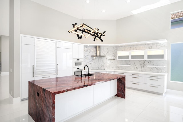 kitchen featuring black electric stovetop, white cabinets, a sink, wall chimney range hood, and modern cabinets