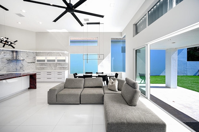 living area with a ceiling fan, a wealth of natural light, visible vents, and a towering ceiling