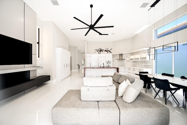 living area featuring light tile patterned flooring, a towering ceiling, visible vents, and a ceiling fan