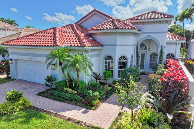 mediterranean / spanish-style house featuring decorative driveway, a tile roof, an attached garage, and stucco siding