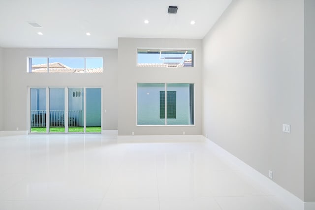 tiled empty room with recessed lighting, visible vents, and a towering ceiling