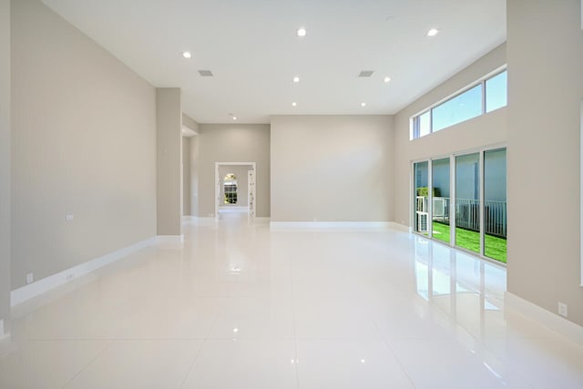 empty room featuring light tile patterned floors, visible vents, baseboards, a high ceiling, and recessed lighting