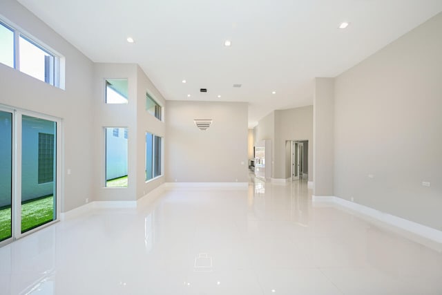 empty room featuring baseboards, a high ceiling, light tile patterned flooring, and recessed lighting