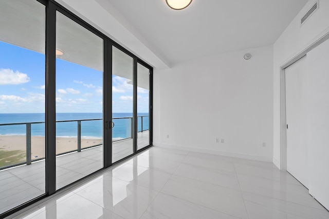 tiled empty room featuring a wall of windows, a water view, visible vents, and baseboards