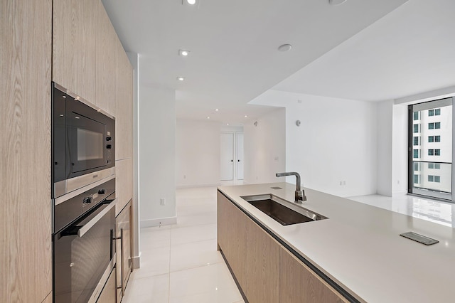 kitchen featuring modern cabinets, stainless steel oven, light brown cabinets, black microwave, and a sink