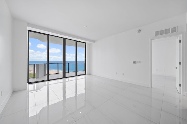 empty room with a wall of windows, visible vents, baseboards, and tile patterned floors