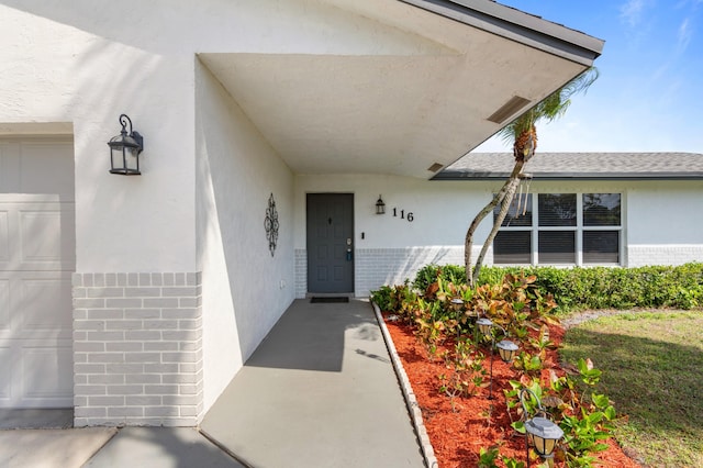 entrance to property with a garage, stucco siding, and brick siding