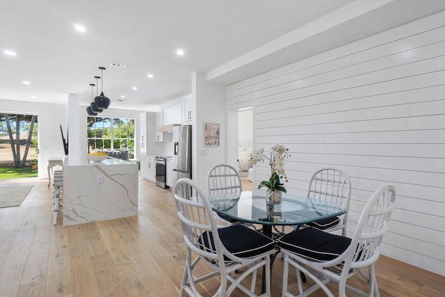 dining space featuring light wood finished floors, visible vents, wood walls, and recessed lighting