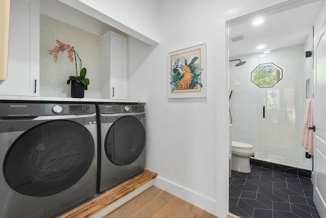 washroom featuring wood finished floors, washing machine and dryer, visible vents, and baseboards