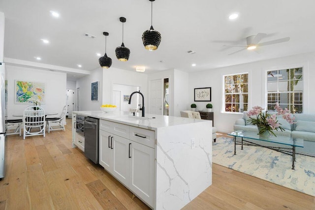 kitchen with light wood finished floors, open floor plan, light stone countertops, white cabinetry, and stainless steel dishwasher