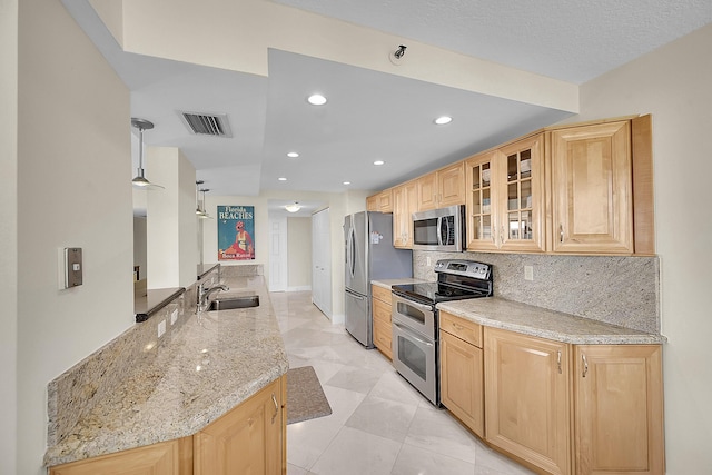 kitchen featuring light stone counters, stainless steel appliances, backsplash, light brown cabinetry, and a sink