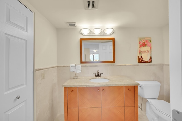 bathroom with tile walls, visible vents, toilet, wainscoting, and vanity