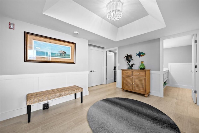 living area with a chandelier, light wood finished floors, and a raised ceiling