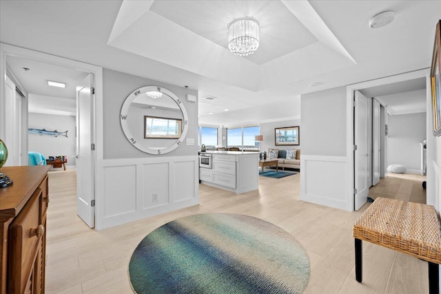 bathroom featuring a tray ceiling, a chandelier, wood finished floors, and wainscoting