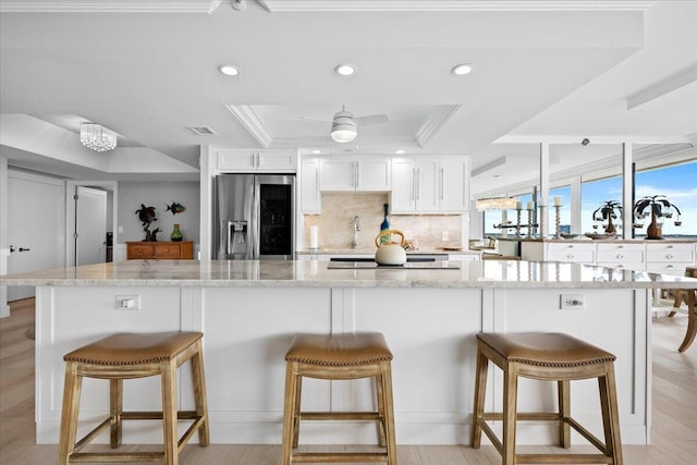 kitchen featuring tasteful backsplash, white cabinets, a raised ceiling, stainless steel fridge with ice dispenser, and recessed lighting