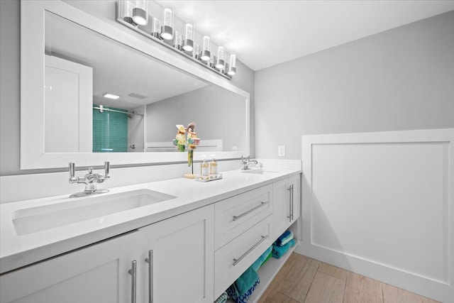 bathroom featuring wood finished floors, a sink, a shower stall, and double vanity