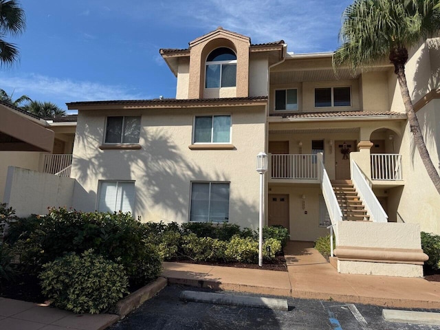 view of front of property with uncovered parking, a tile roof, stairway, and stucco siding