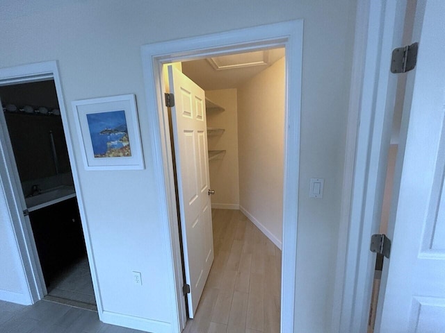 hall with light wood-type flooring, attic access, and baseboards