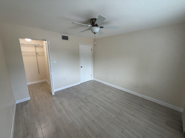 unfurnished bedroom featuring baseboards, visible vents, wood finished floors, a walk in closet, and a closet