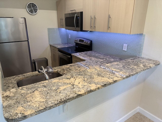 kitchen with stainless steel appliances, a peninsula, a sink, and light stone countertops