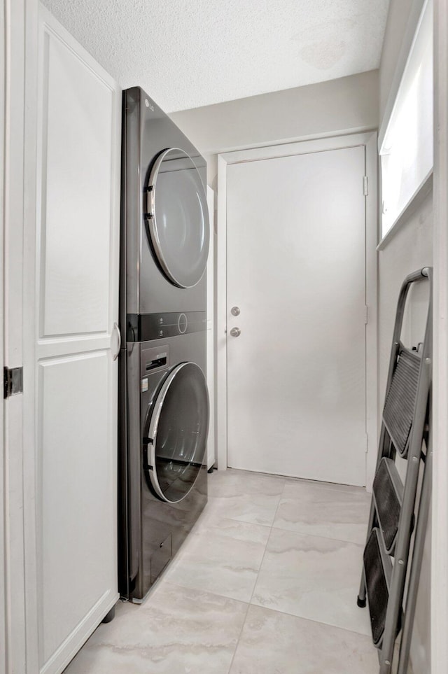 washroom with stacked washing maching and dryer, laundry area, marble finish floor, and a textured ceiling