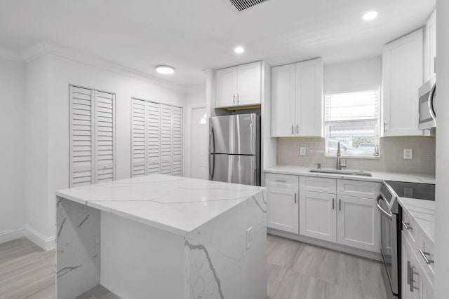kitchen with stainless steel appliances, a sink, a kitchen island, white cabinets, and backsplash