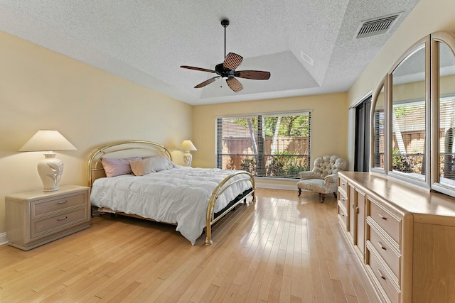 bedroom with visible vents, light wood-style flooring, a textured ceiling, a raised ceiling, and ceiling fan