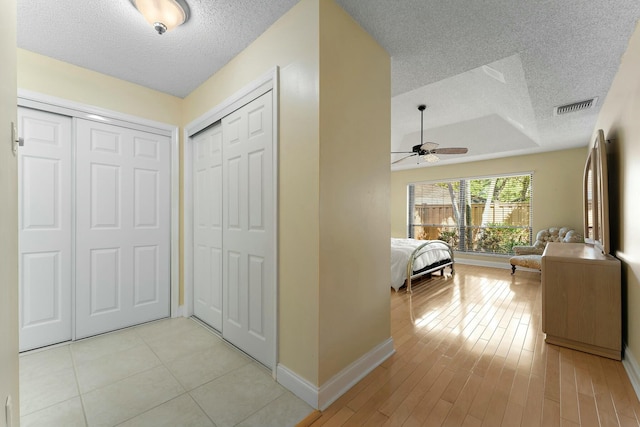 hall with visible vents, light wood-style flooring, a textured ceiling, and baseboards