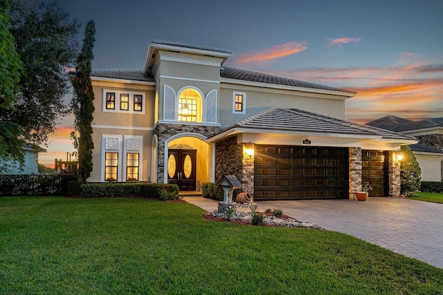 view of front of home featuring stone siding, an attached garage, decorative driveway, french doors, and a front lawn