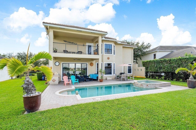 back of property featuring a balcony, a pool with connected hot tub, a lawn, stucco siding, and a patio area