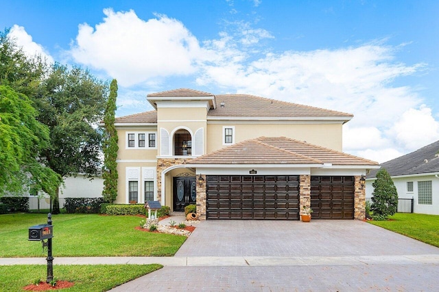 mediterranean / spanish-style home featuring stucco siding, an attached garage, a front yard, stone siding, and driveway