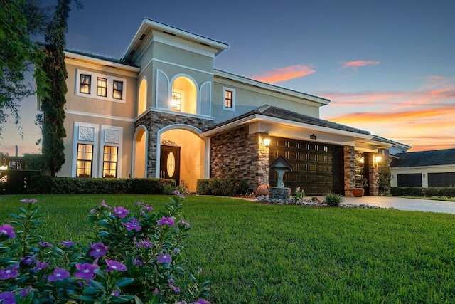 view of front of property with an attached garage, a yard, stone siding, driveway, and stucco siding