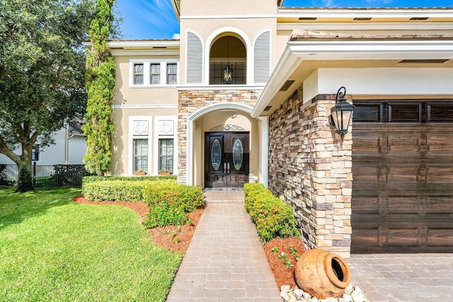 property entrance featuring a garage, a lawn, stone siding, fence, and stucco siding