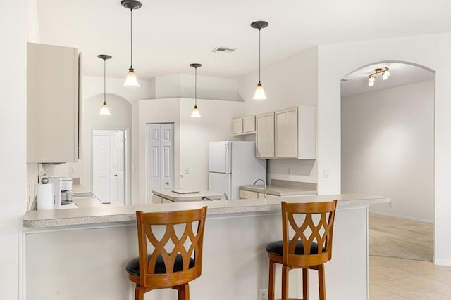 10617 Pine Cone Ln, Fort Pierce, FL 34945 - kitchen featuring arched walkways, visible vents, a breakfast bar, freestanding refrigerator, and light countertops