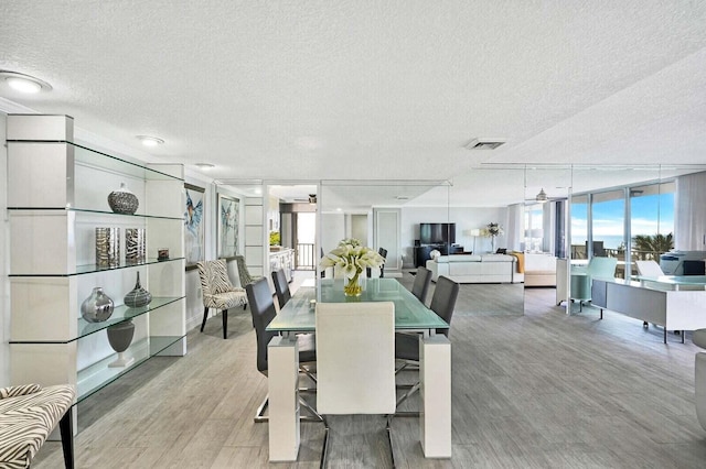 dining room featuring light wood finished floors, a textured ceiling, visible vents, and a ceiling fan