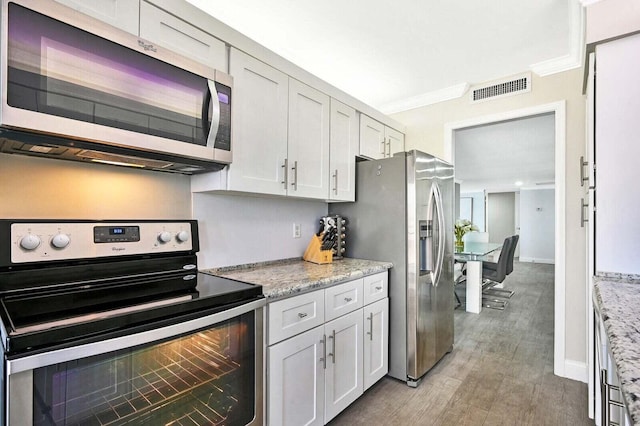 kitchen with crown molding, stainless steel appliances, visible vents, light wood-style floors, and light stone countertops