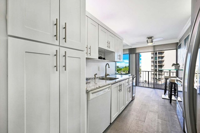 kitchen with light stone counters, white dishwasher, a sink, a ceiling fan, and white cabinetry