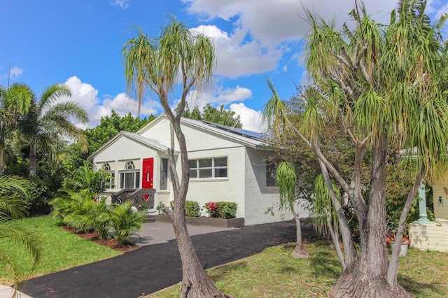 view of front of property featuring driveway, a front lawn, solar panels, and stucco siding