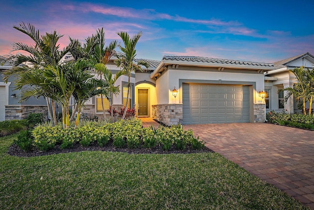 view of front of home featuring decorative driveway, stucco siding, an attached garage, a front yard, and stone siding