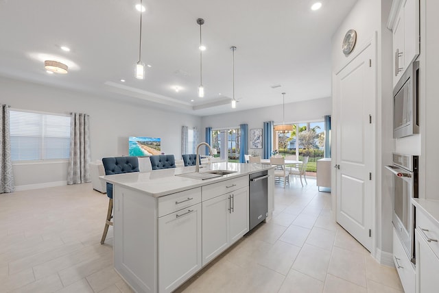 kitchen featuring stainless steel appliances, a sink, white cabinets, open floor plan, and a tray ceiling