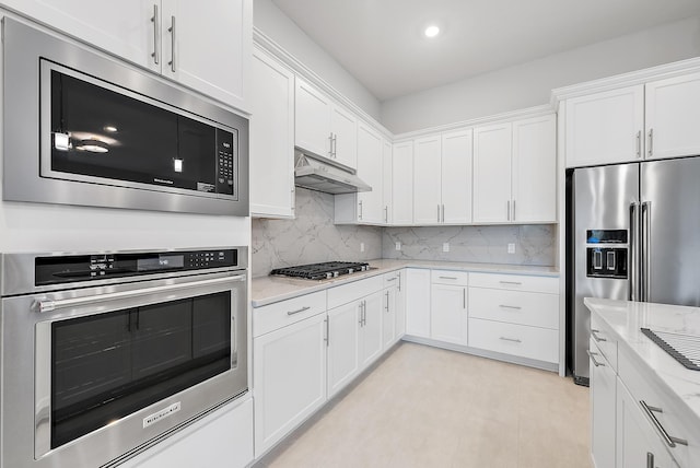 kitchen with stainless steel appliances, decorative backsplash, white cabinetry, and under cabinet range hood