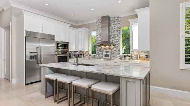 kitchen featuring wall chimney exhaust hood, backsplash, a sink, and built in appliances