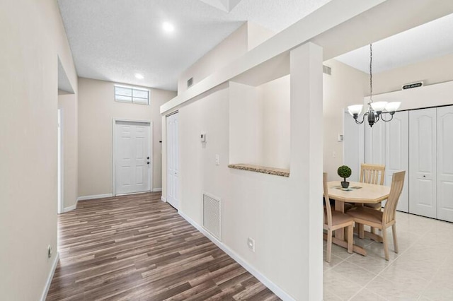 hallway featuring wood finished floors, visible vents, baseboards, and an inviting chandelier