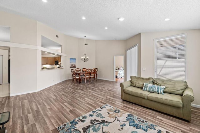 living area featuring a chandelier, a textured ceiling, wood finished floors, and lofted ceiling